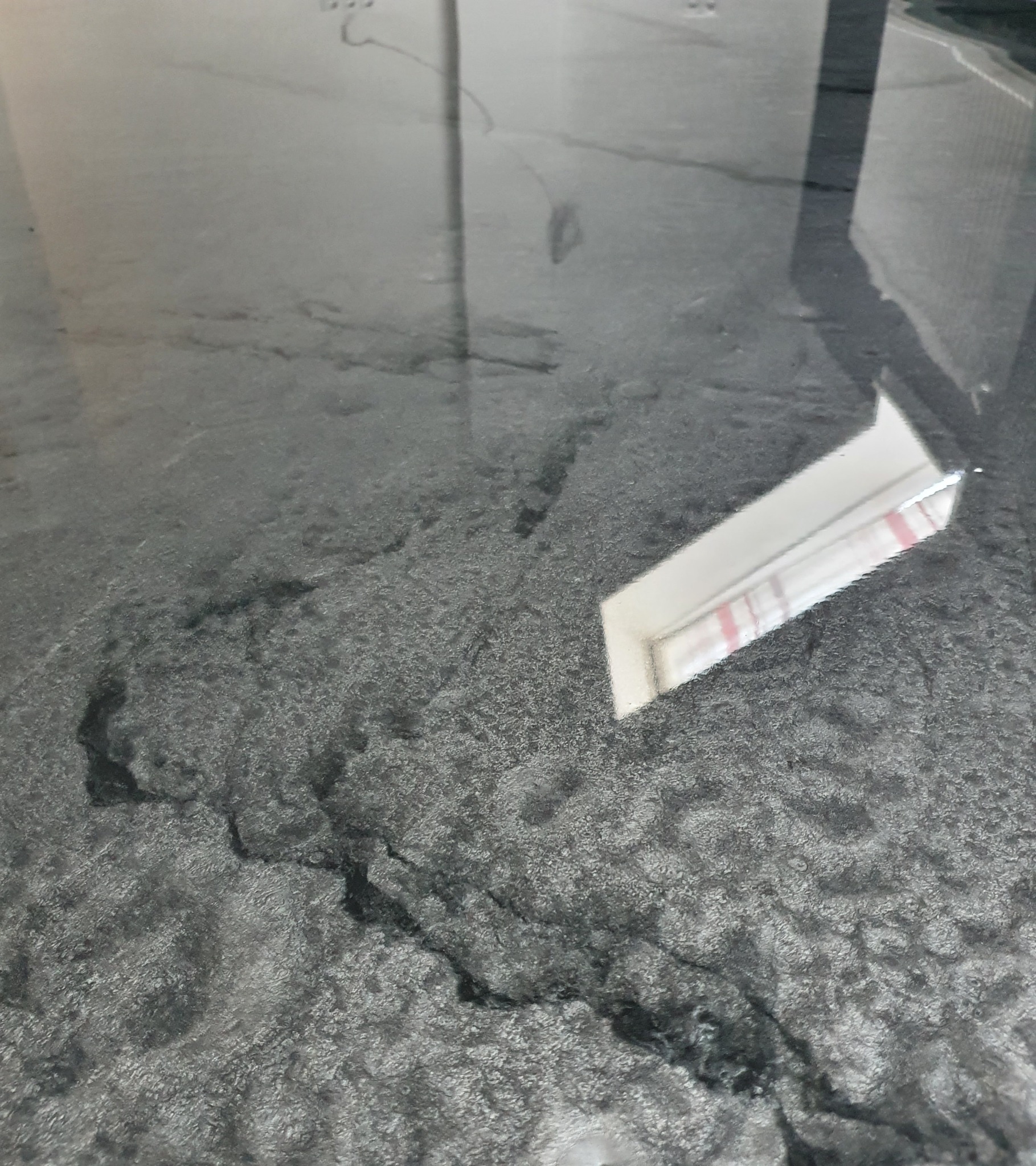 Szara podłoga z żywicy epoksydowej o nieregularnej fakturze, odbijająca światło okna.