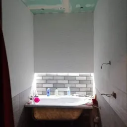 Remont łazienki w Kamionnej: Widok na częściowo wykończoną łazienkę z wanną, płytkami na ścianach i sufitem z płyt karton gips, widoczne niedociągnięcia i brak wykończenia.