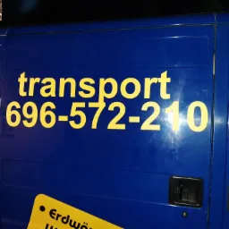 Niebieski van z żółtym napisem 'transport' i numerem telefonu, sfotografowany z bliska, z widocznymi sopelkami lodu w górnym rogu.