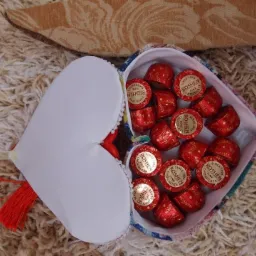 Otwarty, ręcznie szyty woreczek w kształcie serca, wypełniony czekoladkami Roshen w czerwonych papierkach, leżący na puszystym dywanie.