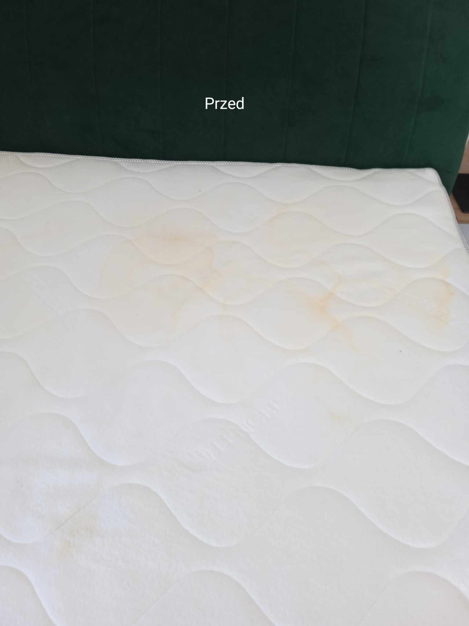 Materac z widocznymi plamami przed czyszczeniem, na tle zielonego zagłówka i z napisem 'Przed'.