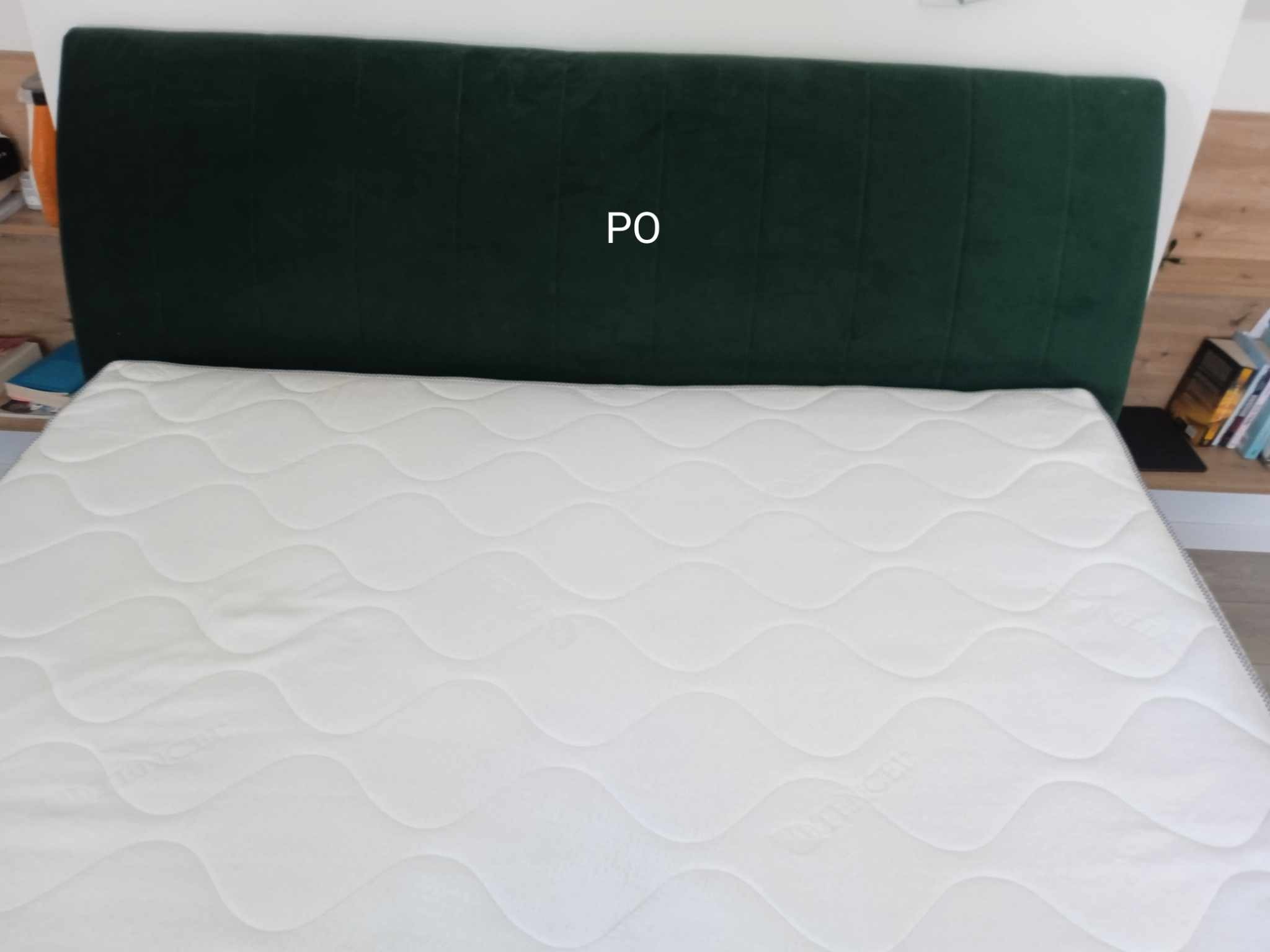 Biały materac z zielonym zagłówkiem w sypialni w Krakowie. Widoczne książki na półce w tle.
