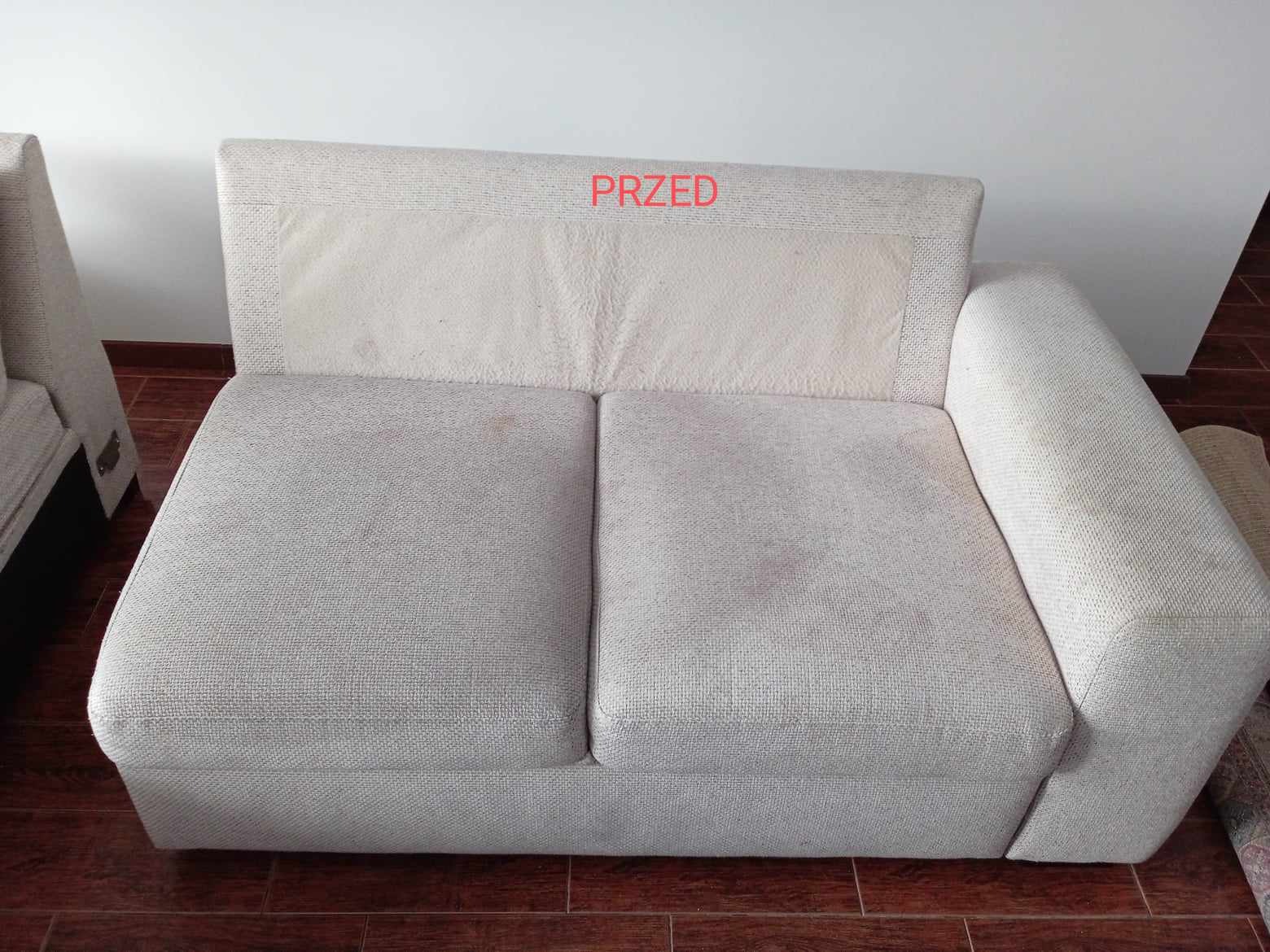 Jasna, dwuosobowa kanapa z widocznymi plamami i zabrudzeniami na siedzisku i oparciu, sfotografowana przed czyszczeniem z napisem 'PRZED' na górze oparcia.