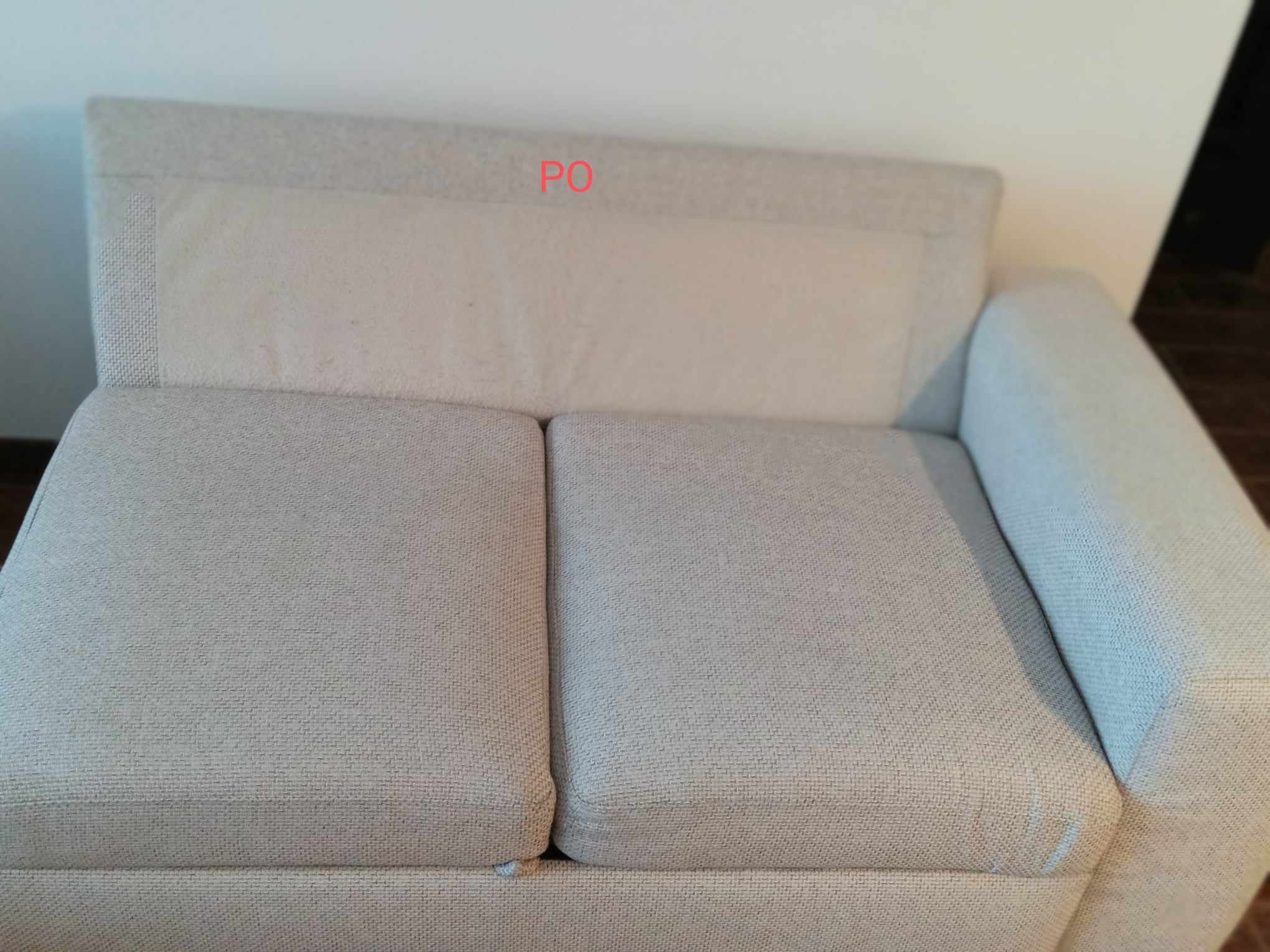 Jasna, dwuosobowa kanapa z wyraźnie widocznymi plamami na oparciu, wymagająca prania tapicerki.