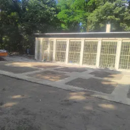 Przygotowanie terenu pod trawnik w ogrodzie z budynkiem oranżerii w tle, widoczne wyznaczone kwatery i materiały budowlane.