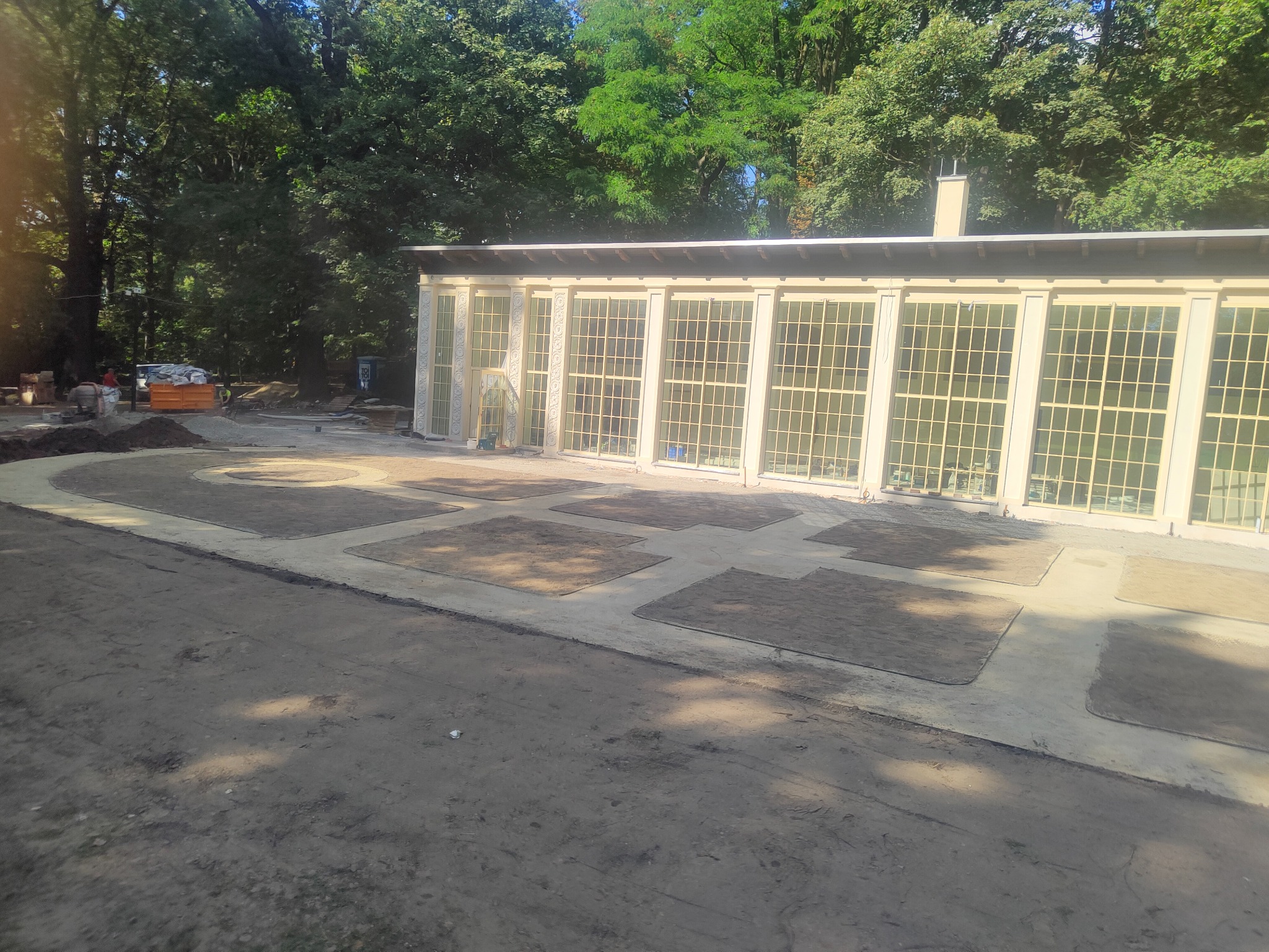 Przygotowanie terenu pod trawnik w ogrodzie z budynkiem oranżerii w tle, widoczne wyznaczone kwatery i materiały budowlane.