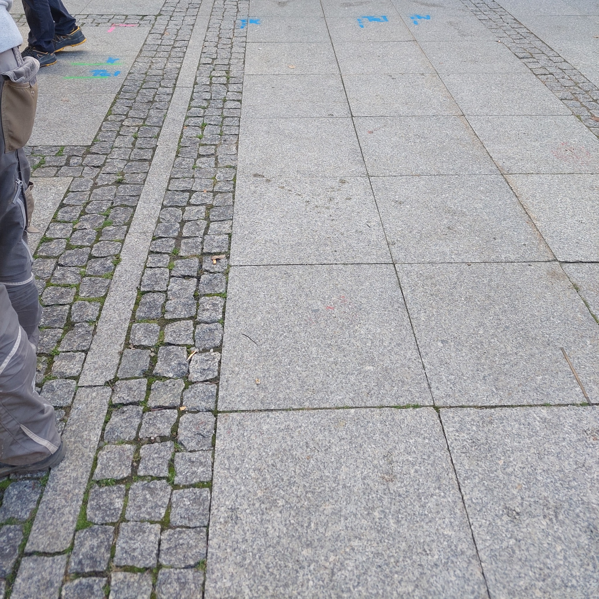 Ułożona nawierzchnia z kostki granitowej i płyt chodnikowych, widoczne fragmenty osoby z boku, z delikatnym mchem między kostkami.