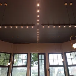 Nowoczesne oświetlenie sufitowe w pomieszczeniu z dużymi oknami: kombinacja szynoprzewodów z reflektorami i wiszących lamp kulistych z metalowymi oprawami.