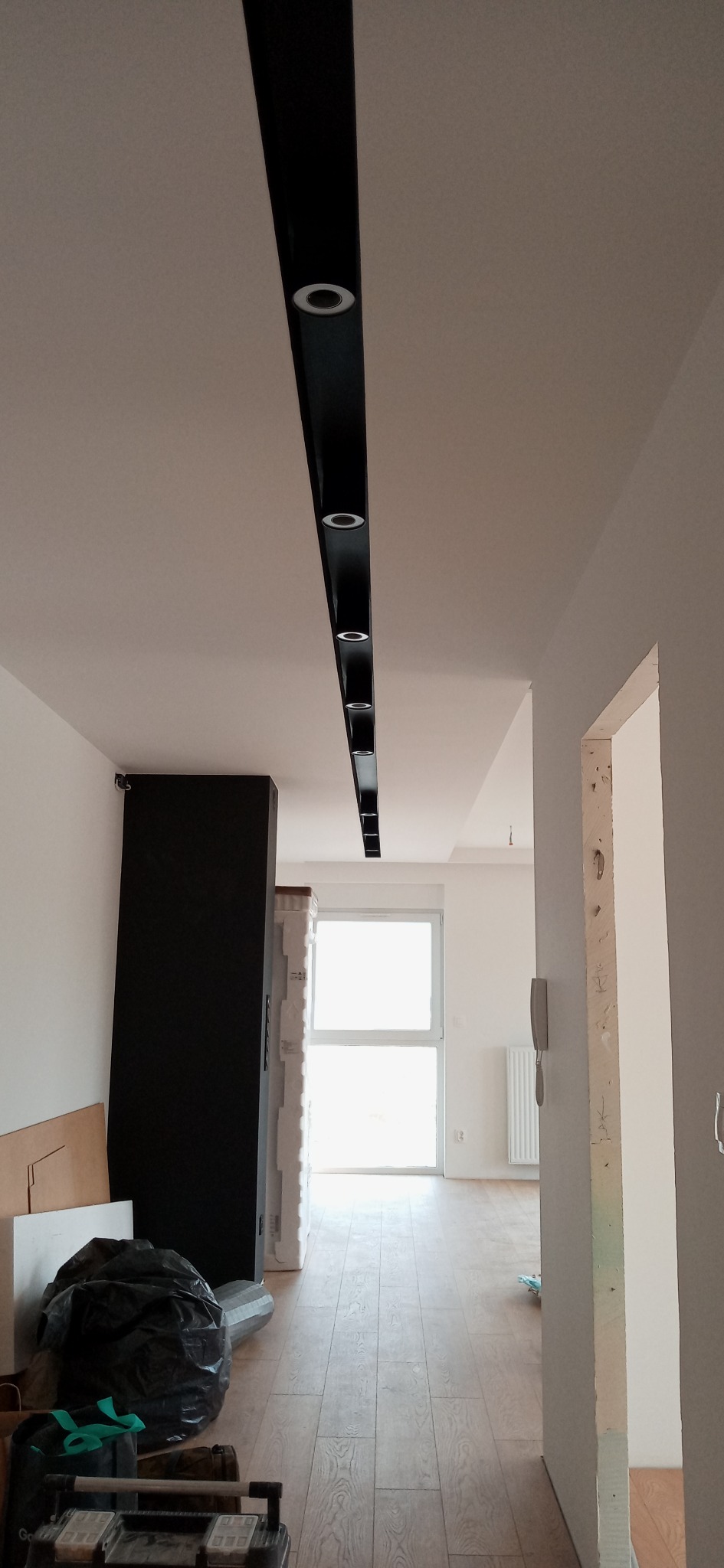 Czarna listwa oświetleniowa z punktowymi reflektorami LED zamontowana na suficie w mieszkaniu we Wrocławiu, widoczne narzędzia i materiały budowlane na podłodze, wnętrze w trakcie wykańczania.