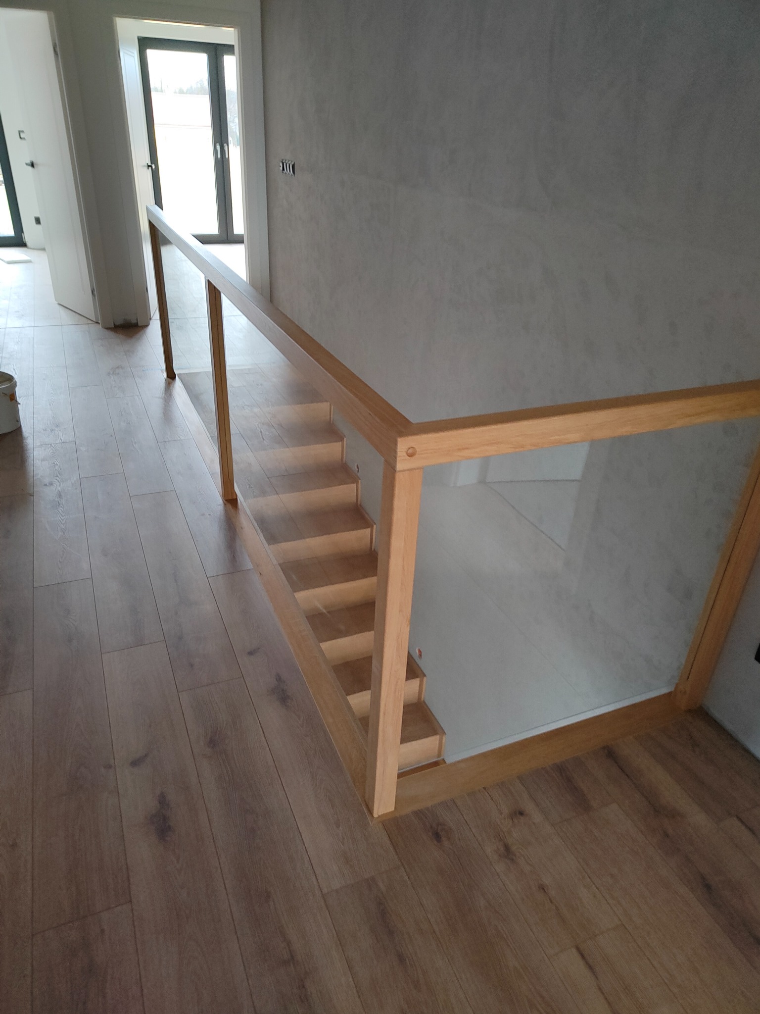 Nowoczesne schody z jasnego drewna z przeszkloną balustradą, widok z góry na drewnianą podłogę