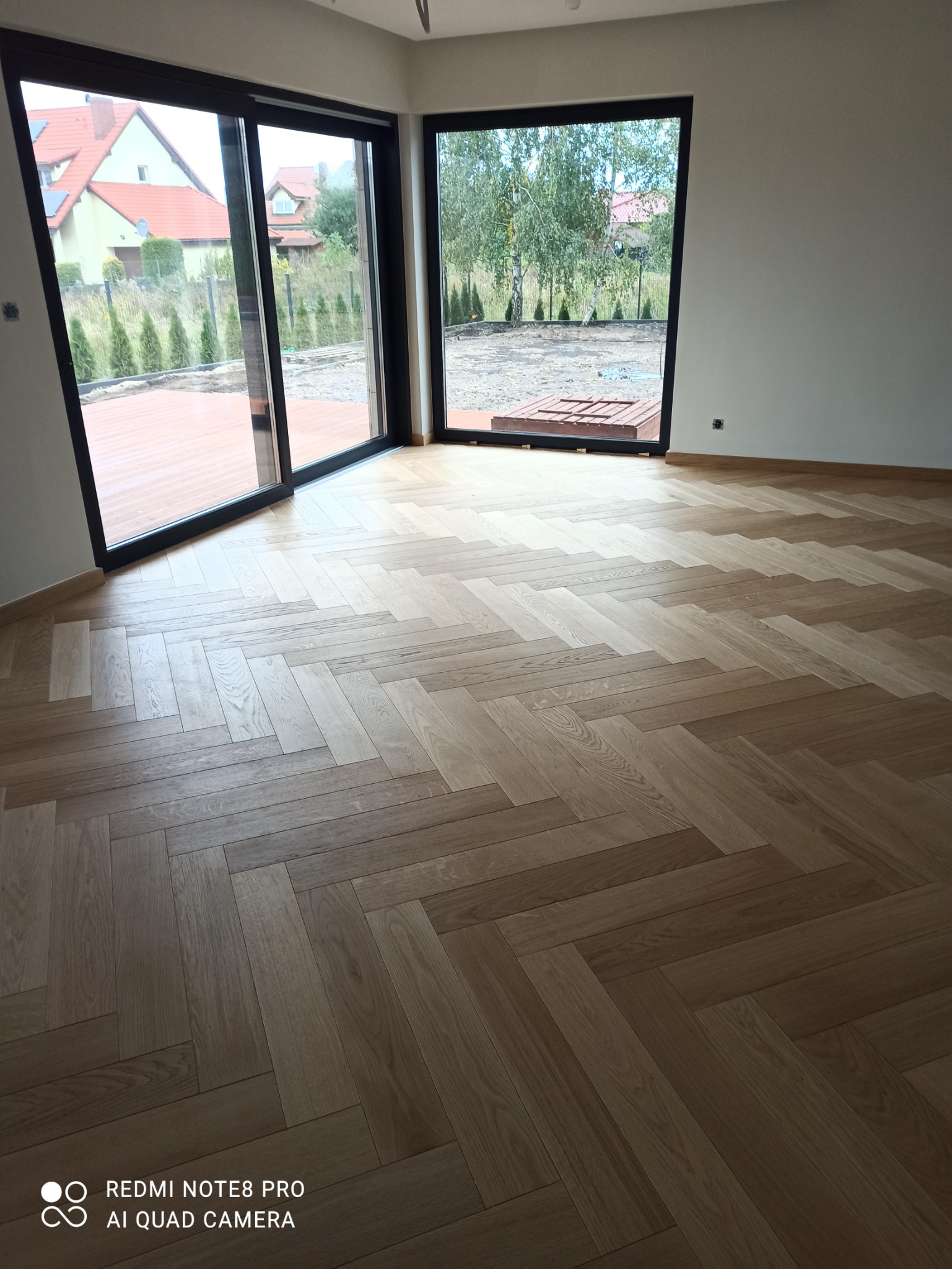 Jasne panele ułożone we wzór jodełki francuskiej w przestronnym, jasnym pokoju z dużymi oknami przesuwnymi wychodzącymi na ogród.