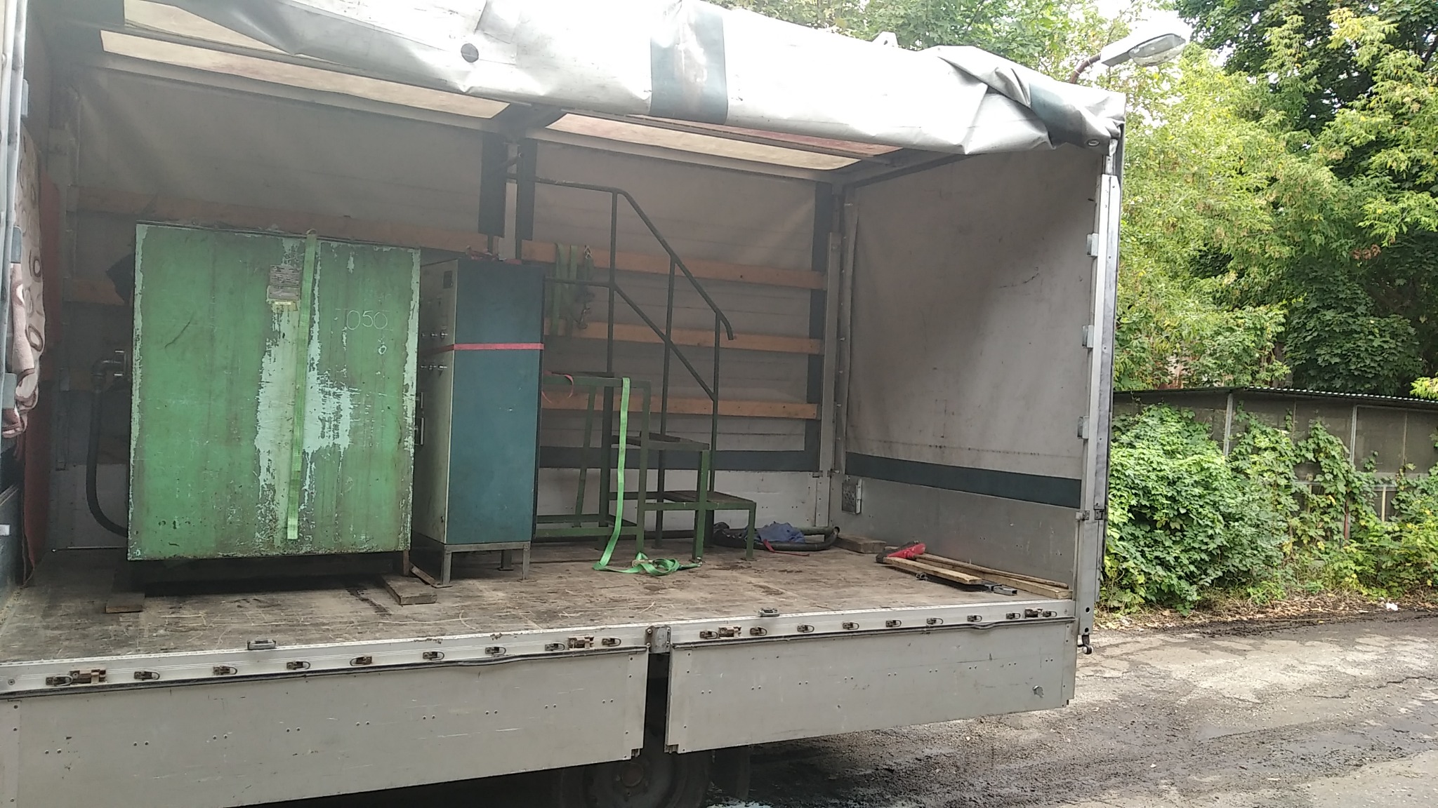 Wnętrze skrzyni ładunkowej ciężarówki w Łasinie, z załadowanymi maszynami przemysłowymi, zabezpieczonymi pasami transportowymi.