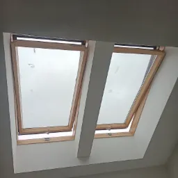 Dwa okna dachowe z drewnianą ramą, zamontowane w poddaszu z wykończonymi ścianami, widoczne z dołu.