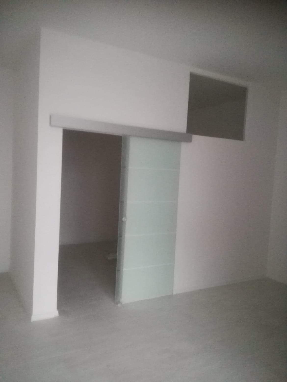 Szklane drzwi przesuwne z poziomymi paskami w nowo wykończonym, pomalowanym na biało pomieszczeniu z widoczną wnęką w ścianie.