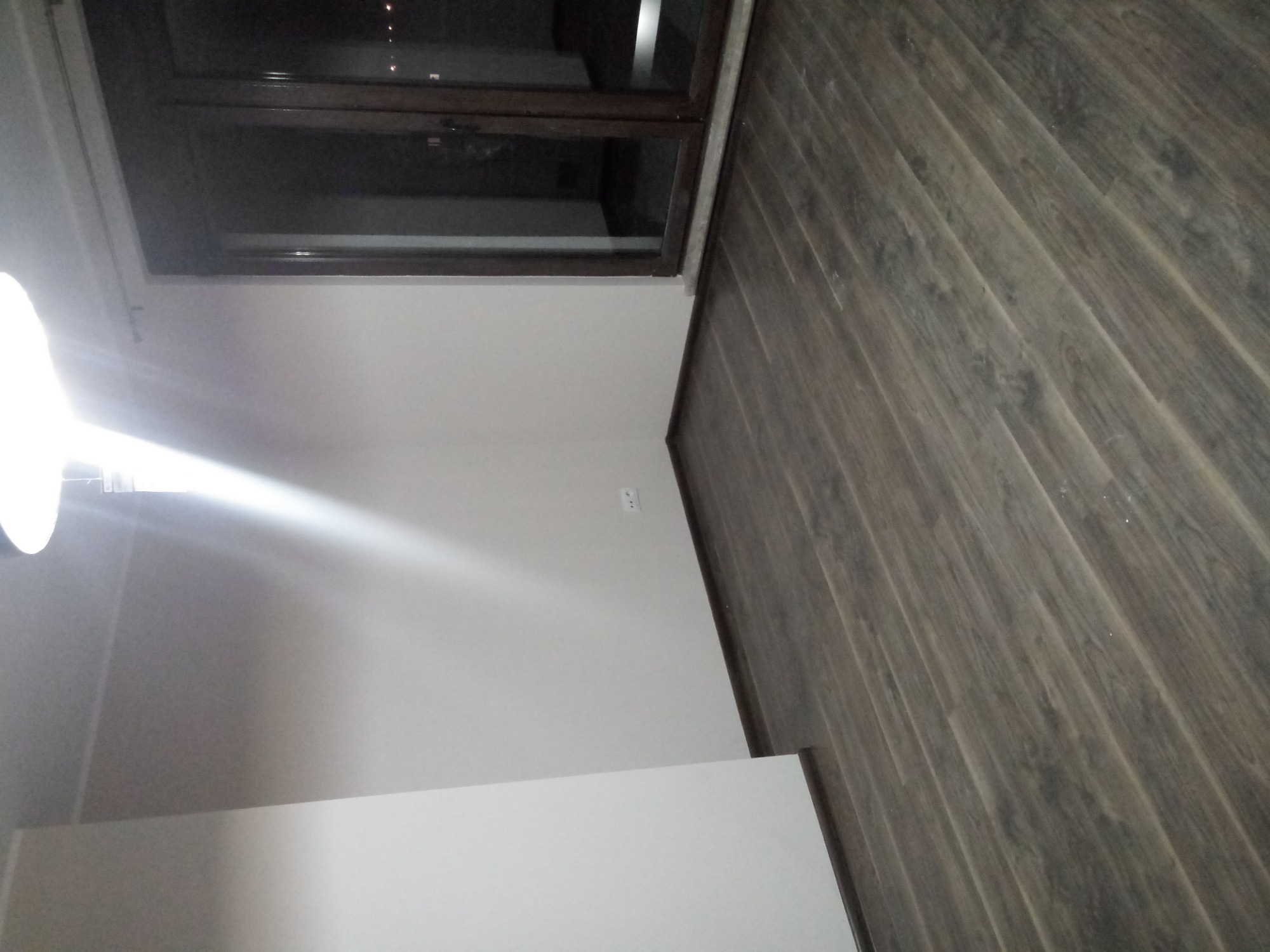 Nowo położona, ciemnobrązowa podłoga laminowana z widocznym oknem i świeżo pomalowanymi ścianami w jasnym odcieniu, z widocznym gniazdkiem elektrycznym.