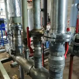 System rur ze stali nierdzewnej z zaworami i izolacją, widoczne ślady spawania i łączenia elementów, zamontowany wewnątrz budynku.