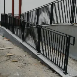 Zewnętrzna, dwupoziomowa, czarna balustrada z metalu przy budynku w Sułowie, zamontowana na betonowym podjeździe dla osób z niepełnosprawnościami, widoczna z perspektywy ziemi, teren budowy.