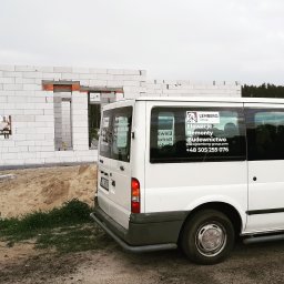 LEMBERG Group - Budynek w trakcie wznoszenia ścian z białych bloczków, na pierwszym planie biały bus z naklejkami reklamowymi firmy budowlanej.