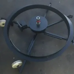 Metalowa konstrukcja obrotowa na kółkach, prawdopodobnie element bramy lub innego urządzenia, z centralnym łożyskiem i ramionami wspierającymi.