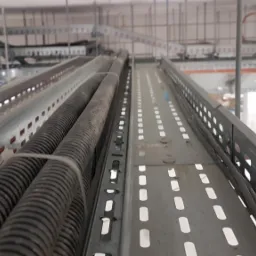 Metalowe korytka kablowe z przewodami w peszlu, zamocowane pod sufitem w przestrzeni technicznej budynku.