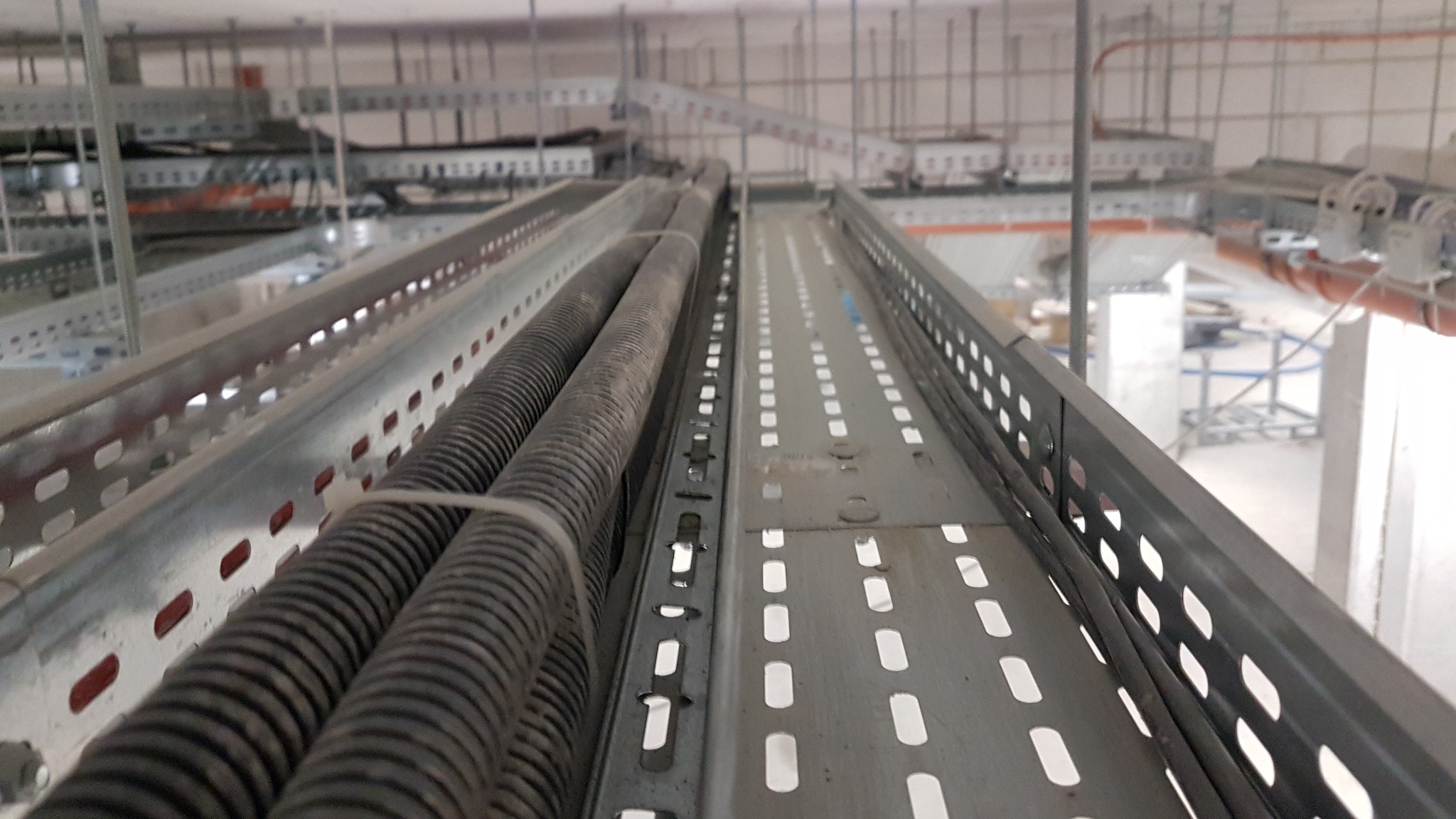 Metalowe korytka kablowe z przewodami w peszlu, zamocowane pod sufitem w przestrzeni technicznej budynku.