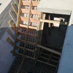 Zbrojenie i szalunek drewniany przygotowany do zalania betonem, widok z góry na budowę fundamentów budynku z bloczków betonowych, w tle wiadro i poziomica.