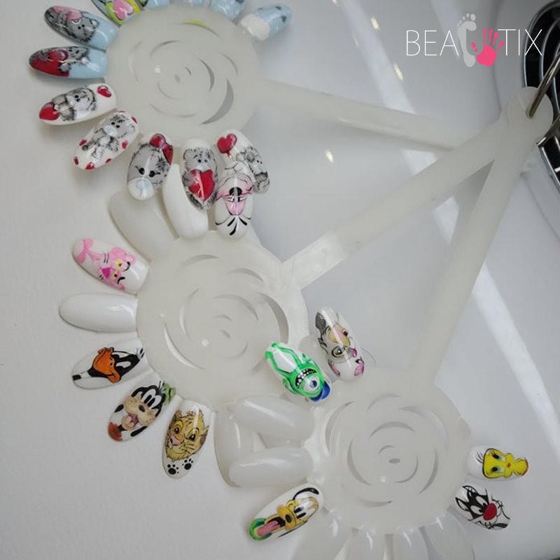 Prezentacja wzorów zdobień paznokci na plastikowych paletach, z motywami kreskówkowymi takimi jak: koty, Tweety, Goofy, Daffy Duck, Simba, Mike Wazowski, Pink Panther i inne postacie.