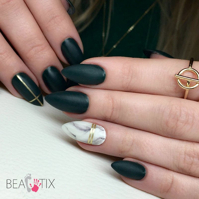 Eleganckie, matowe, ciemnozielone paznokcie w kształcie migdała z geometrycznymi złotymi akcentami oraz marmurkowy wzór na jednym paznokciu, uzupełnione złotym pierścionkiem.