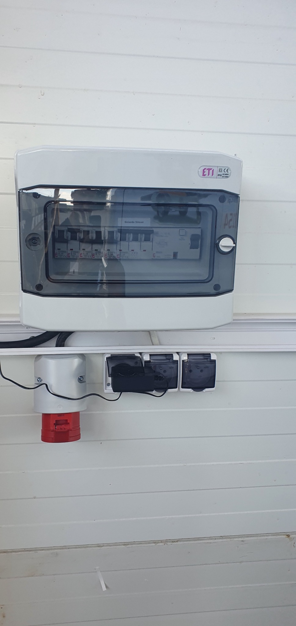 Zamknięta skrzynka rozdzielcza ETI z bezpiecznikami i gniazdami siłowymi zainstalowana na białej ścianie w Ozimku.