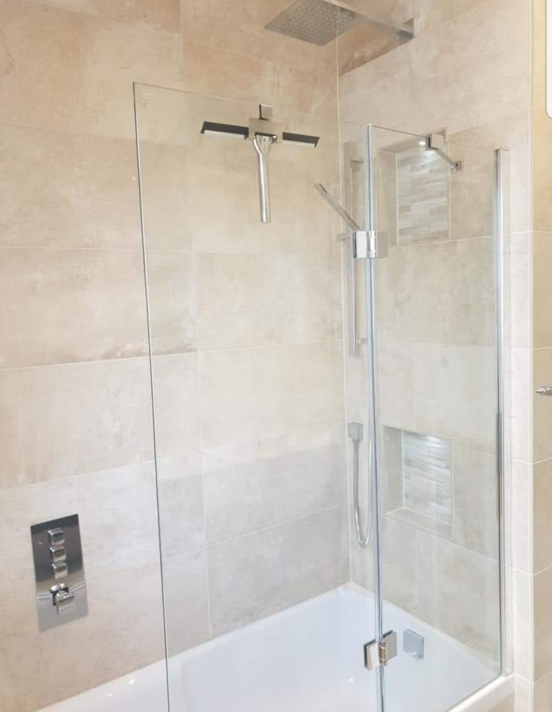 Nowoczesna łazienka z beżowymi płytkami, szklanym parawanem nawannowym z chromowanymi zawiasami, deszczownicą i wnęką wyłożoną mozaiką.