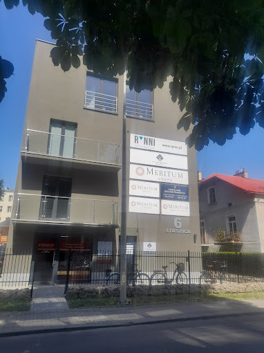 Elewacja budynku biurowego z szyldami firm finansowych, w tle drzewo i rower oparty o ogrodzenie.