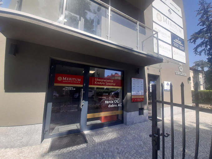 Wejście do biura firmy oferującej ubezpieczenia, kredyty i leasingi, z widocznymi logotypami firmy na elewacji budynku.