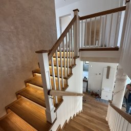 Perfekt-Home - Nowoczesne schody z drewna z podświetleniem LED na stopniach, białe balustrady z drewnianymi poręczami. Widok z góry na dół, wnętrze domu w tle.