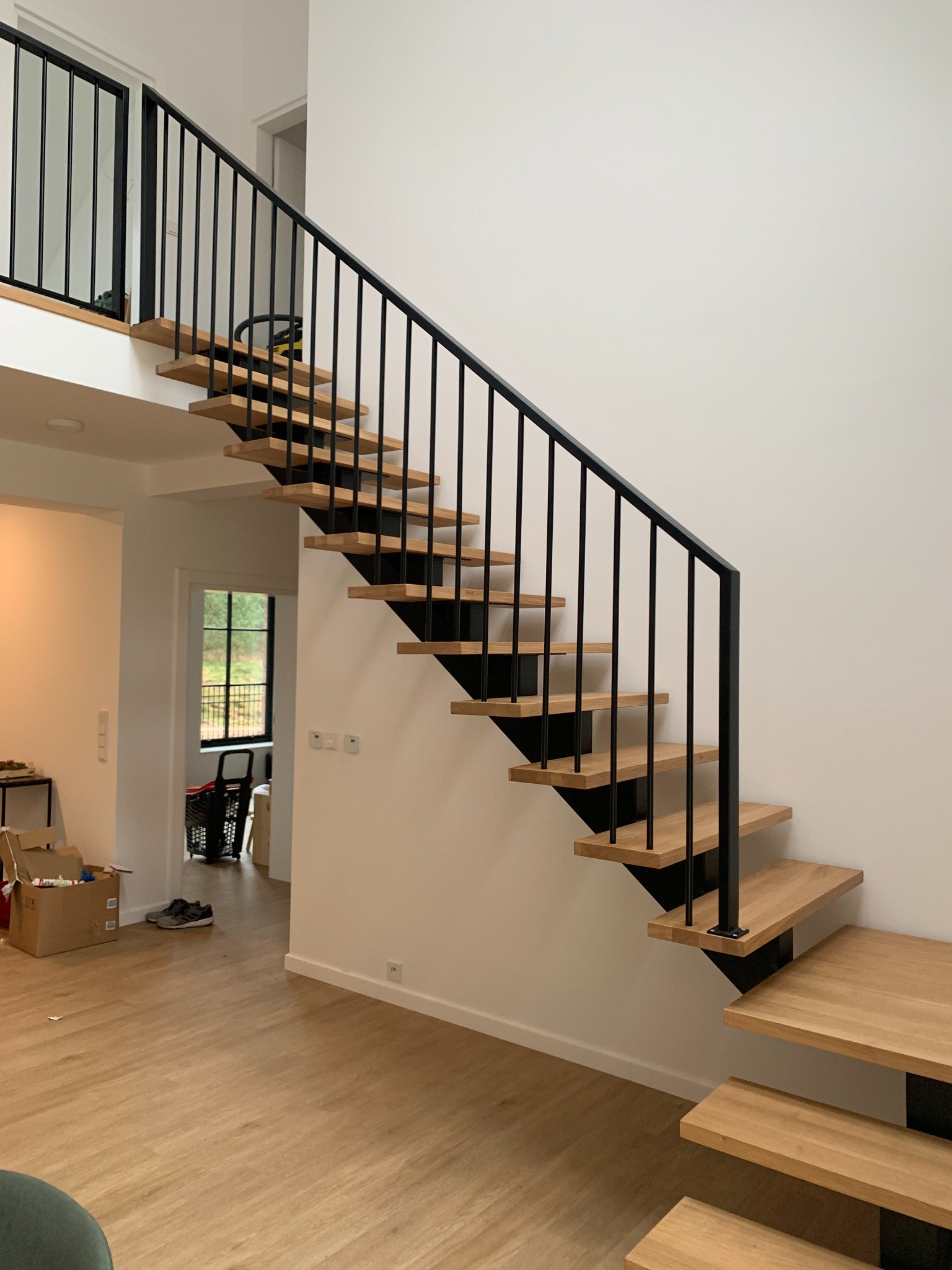 Nowoczesne schody z drewnianymi stopniami i czarną, metalową balustradą w jasnym wnętrzu. Minimalistyczny design, widok z dołu, naturalne światło.