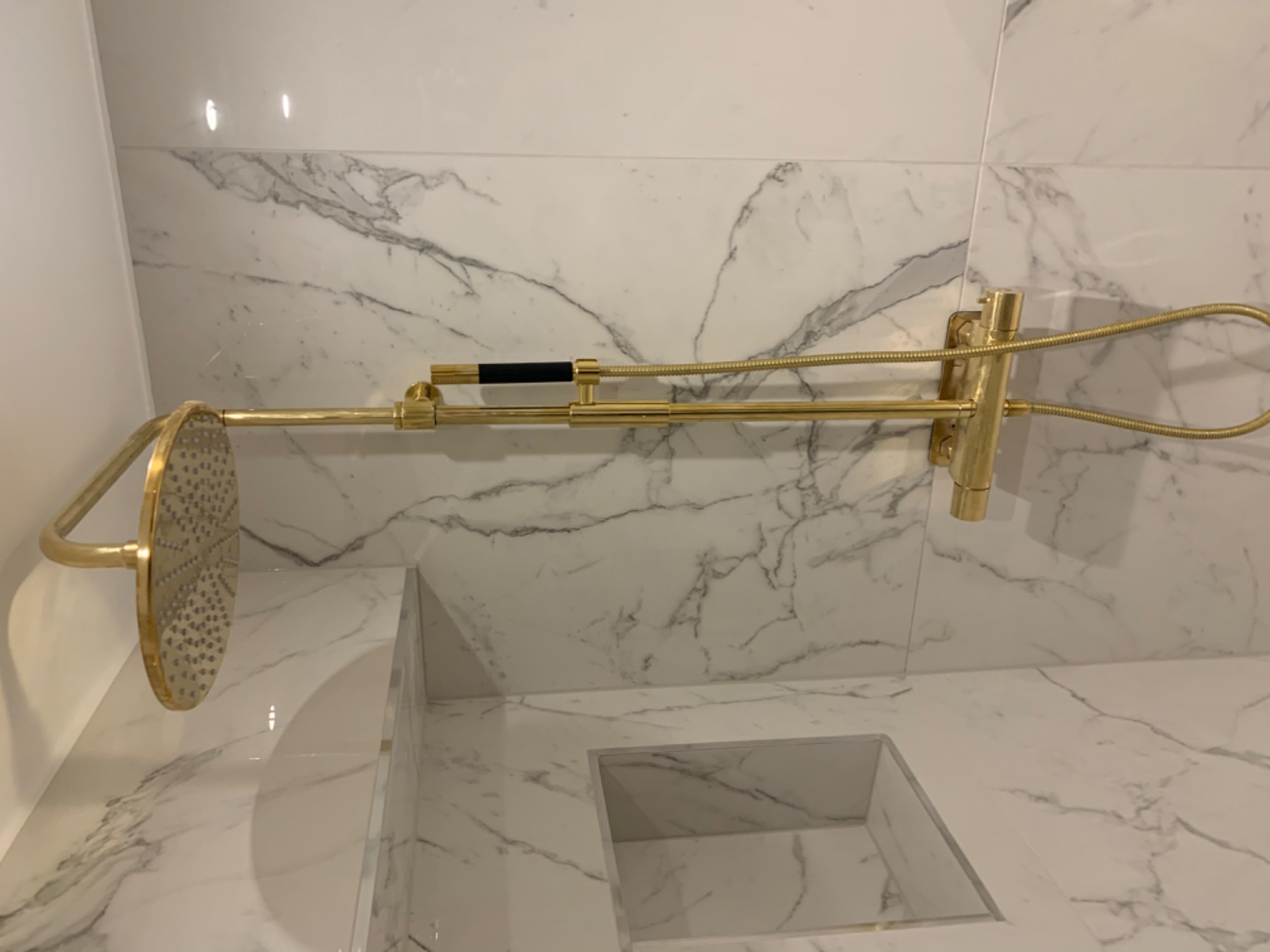 Złoty zestaw prysznicowy z deszczownicą na ścianie z białego marmuru w nowoczesnej łazience.