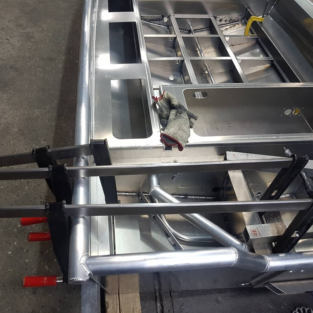 Aluminiowa rama konstrukcyjna w trakcie spawania, widoczne spawy, zaciski stolarskie i robocze rękawice ochronne.