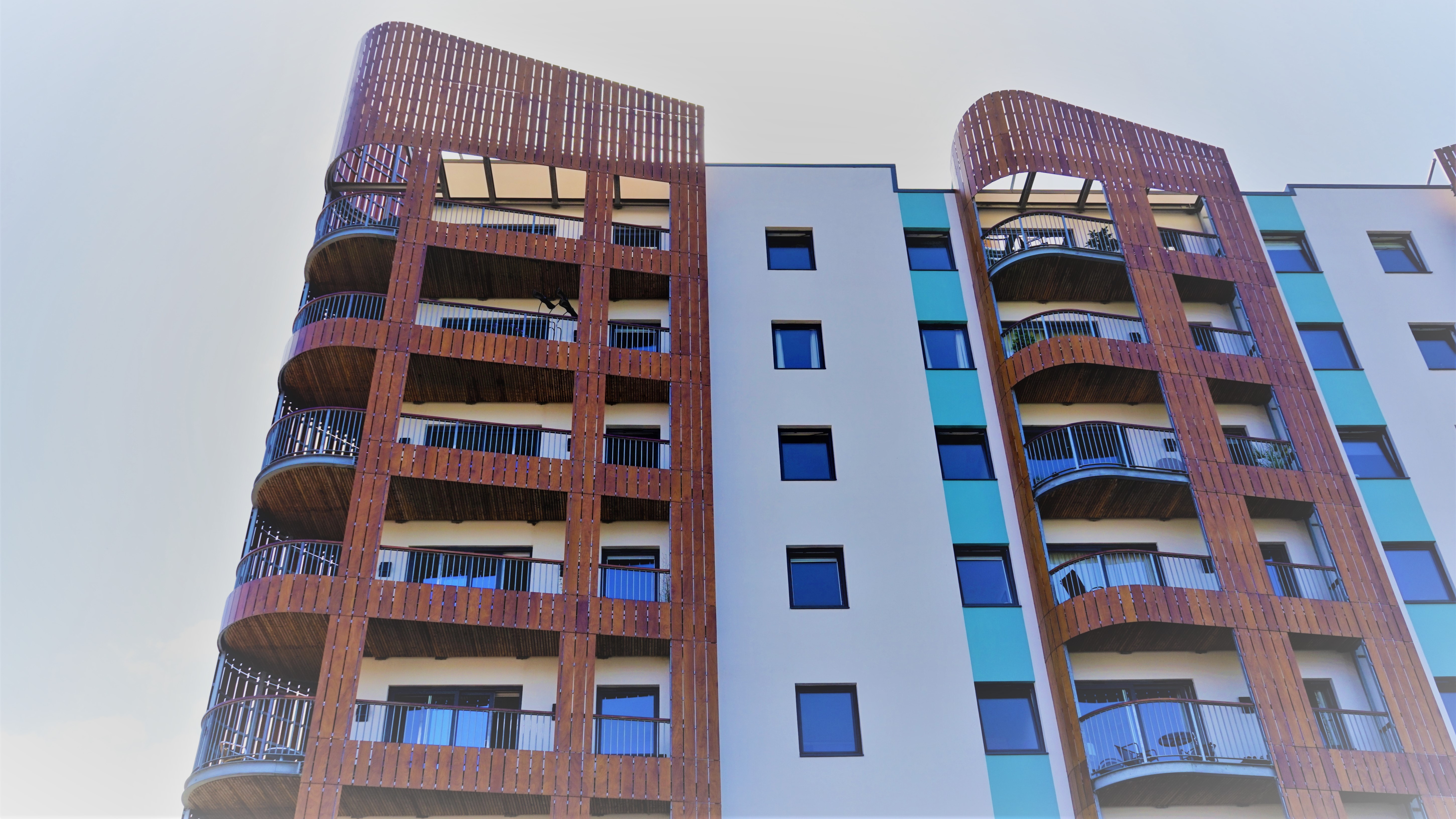 Fasada nowoczesnego budynku mieszkalnego z drewnianymi elementami dekoracyjnymi balkonów i rzędami regularnie rozmieszczonych okien.