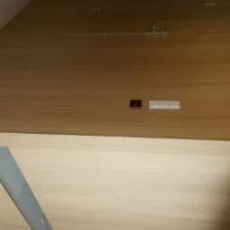 Drewniana zabudowa pod skosem ze schowkiem, umywalką, włącznikami światła i gniazdkiem elektrycznym.