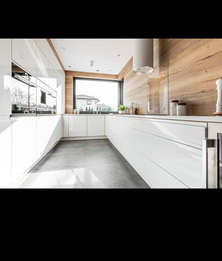 Nowoczesna kuchnia w kształcie litery U z białymi, lakierowanymi frontami, drewnianą okładziną ściany i dużym oknem z widokiem na dom.