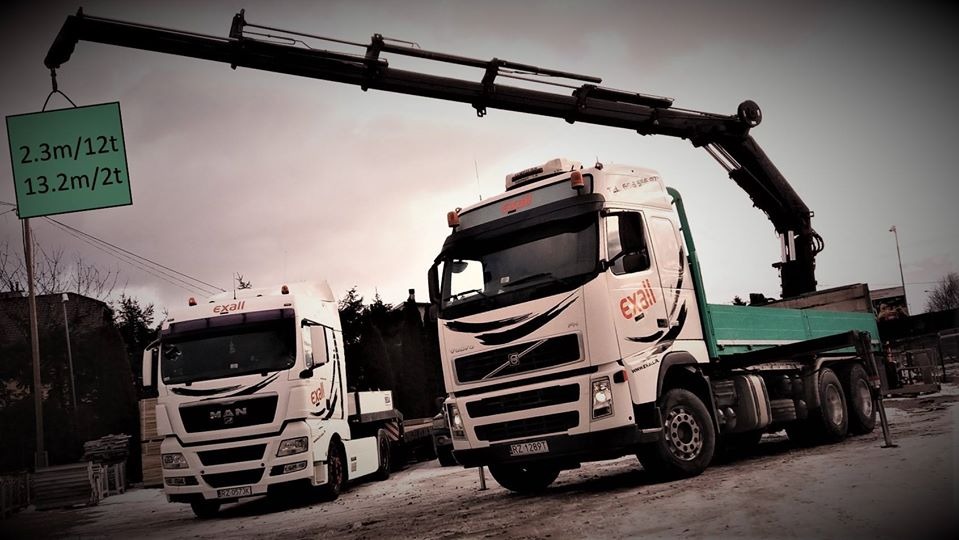 Dwa białe samochody ciężarowe marki MAN i Volvo z dźwigiem hydraulicznym w tle, na jednym z nich widnieje tablica informacyjna o dopuszczalnej masie i wysokości.