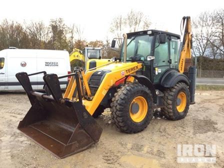 Żółta koparko-ładowarka marki Terex z łyżką z przodu, stojąca na placu budowy, w tle biały bus Wacker Neuson i fragment innej maszyny budowlanej.