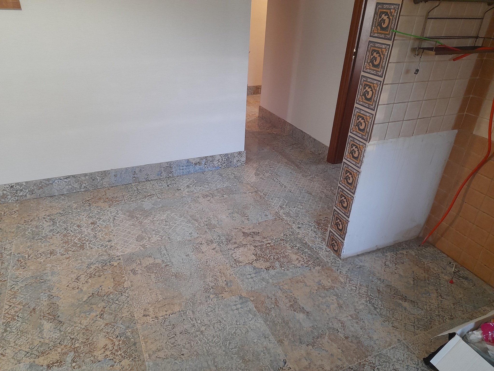 Remont łazienki w Morągu: położona podłoga z wzorzystych płytek, widoczny fragment ściany z dekoracyjnym cokołem i fragment ściany z przygotowanymi płytkami do położenia.