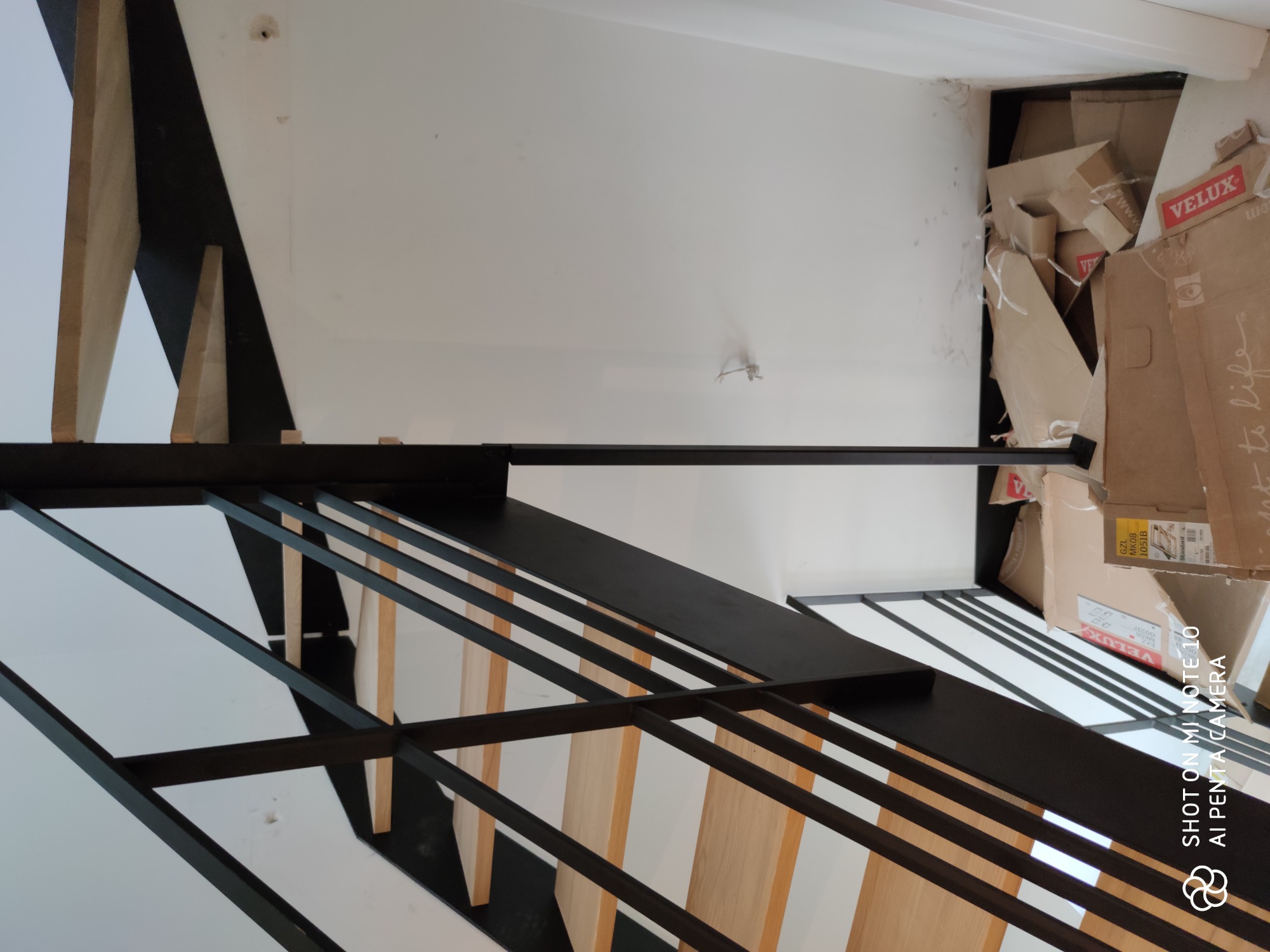 Nowoczesne, drewniane schody z czarną, metalową balustradą w trakcie montażu, widoczne kartony po produktach VELUX w rogu pomieszczenia.