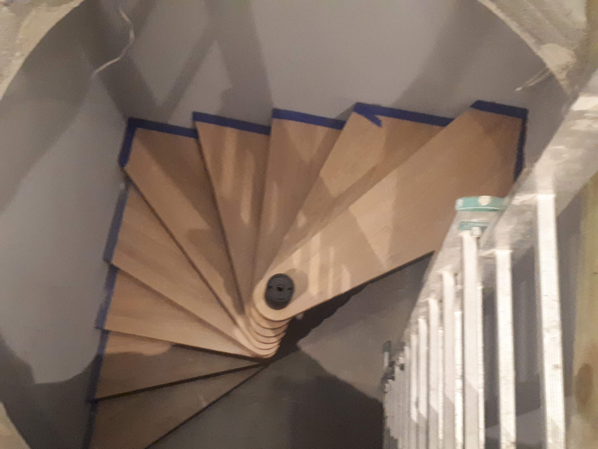 Wewnętrzne, spiralne schody drewniane w trakcie montażu, zabezpieczone niebieską taśmą malarską, widoczne z góry, obok drabina.