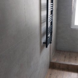 DRAGO BUD - Minimalistyczna łazienka po remoncie: szare, duże płytki na ścianach, drewnopodobne płytki na podłodze, czarny grzejnik drabinkowy, kabina prysznicowa.