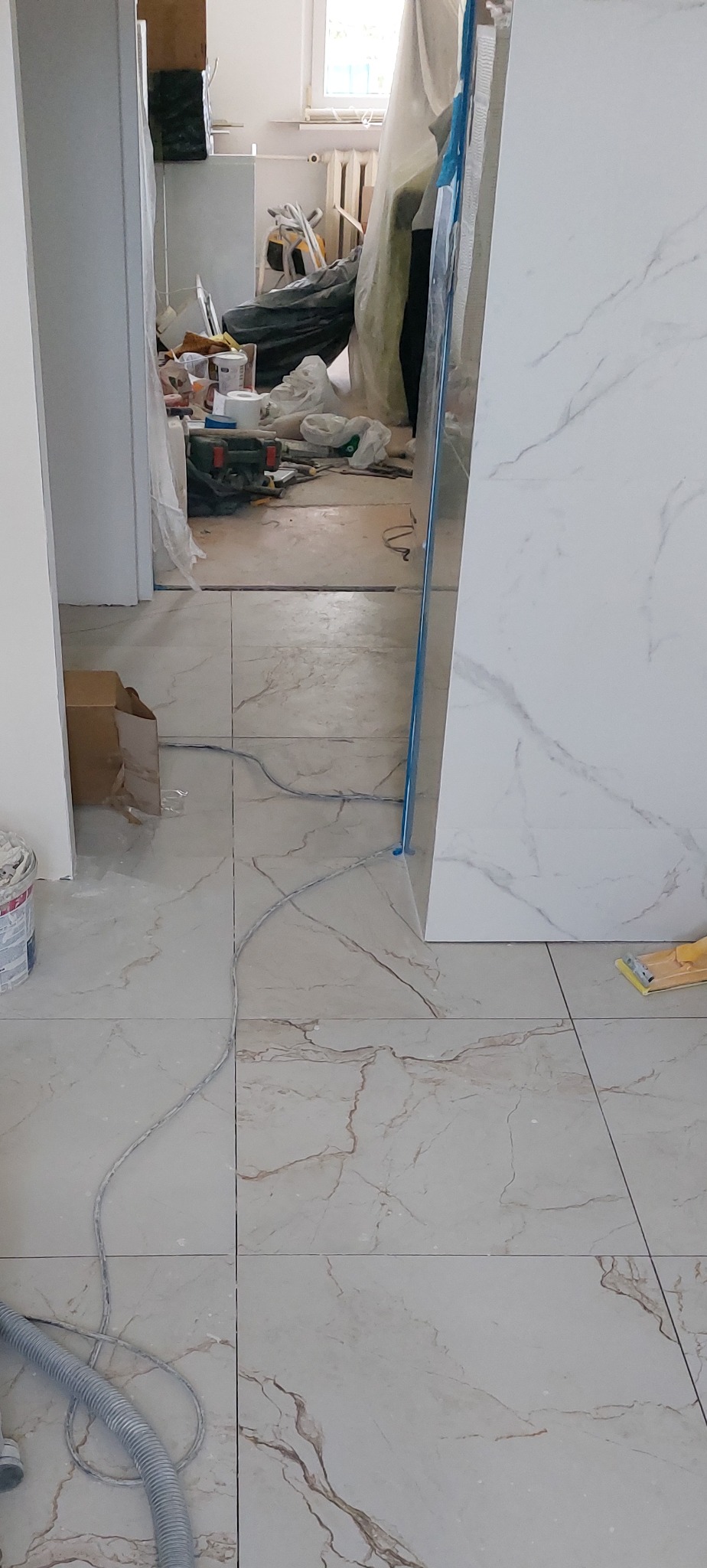 Ułożone płytki podłogowe imitujące marmur w trakcie prac wykończeniowych. W tle widoczne narzędzia i materiały budowlane, co wskazuje na trwający remont.