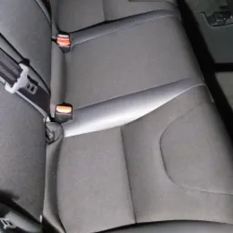 Czarne, materiałowe tylne siedzenie samochodowe z pasami bezpieczeństwa, widoczne detale przeszyć i logo firmy czyszczącej w prawym dolnym rogu.