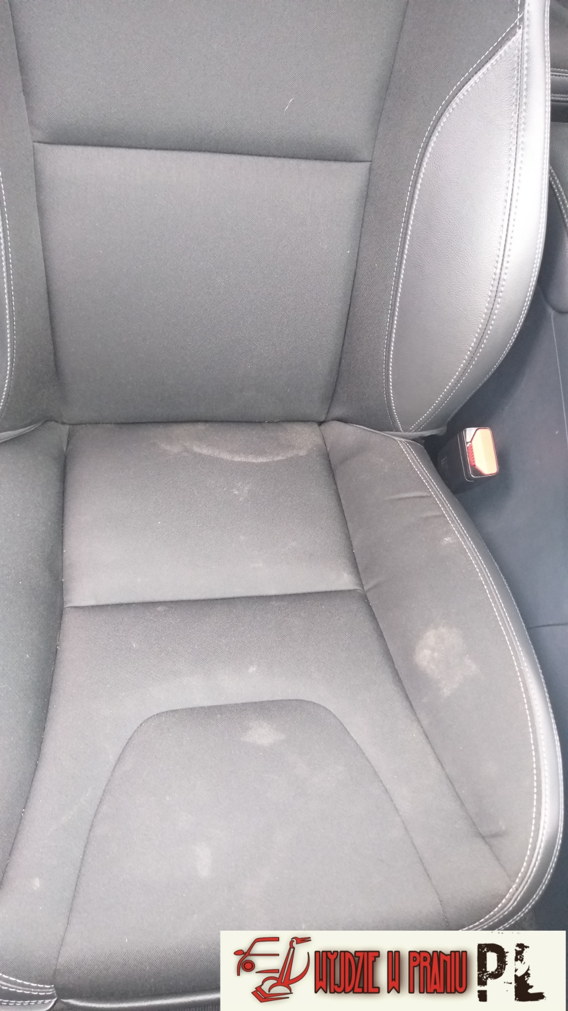 Brudny, szary fotel samochodowy z plamami przed czyszczeniem, widoczny pas bezpieczeństwa, ujęcie z góry.