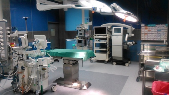 Wyposażona sala operacyjna z lampami zabiegowymi Maquet, stołem operacyjnym przykrytym zielonym materiałem i aparaturą medyczną.