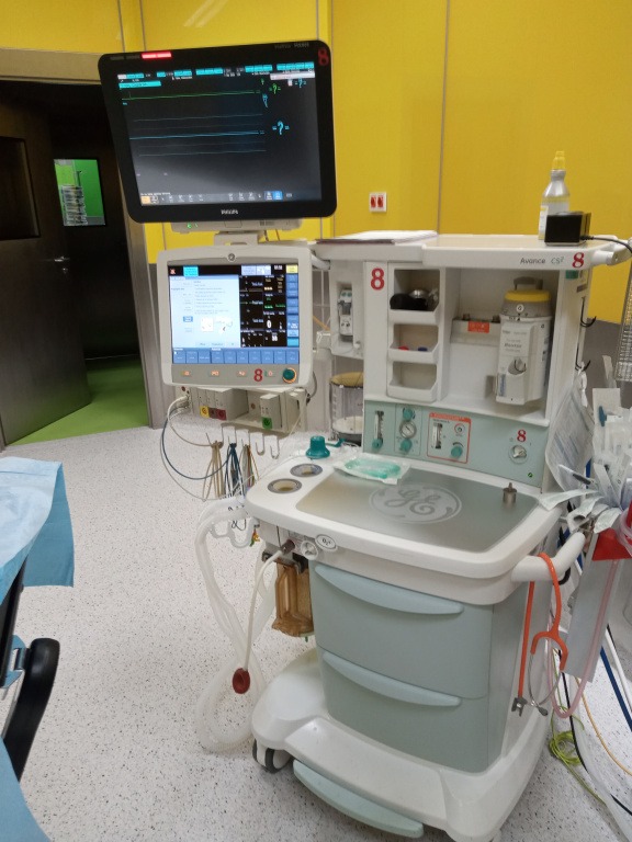 Aparat do znieczulenia Avance CS2 z monitorami wyświetlającymi parametry życiowe pacjenta w pomieszczeniu o żółtych ścianach.